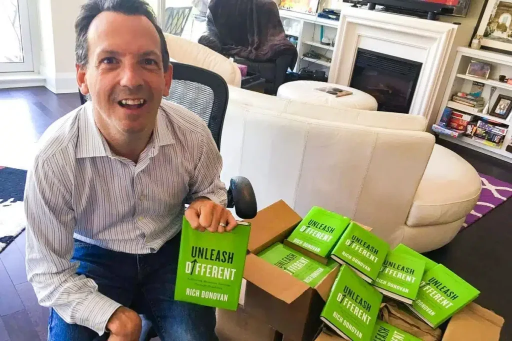 A man sitting in a chair, holding a box of books, representing the commitment to disability employment in Alberta.